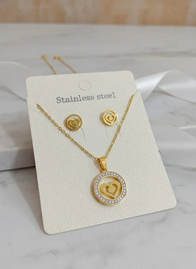 Gold necklace and earrings set on a white card with 'Stainless steel' text, displayed on a marble surface.