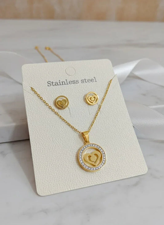 Gold necklace and earrings set on a white card with 'Stainless steel' text, displayed on a marble surface.
