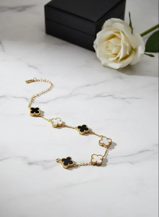 Gold bracelet with black and white stones on a marble surface with a white rose.