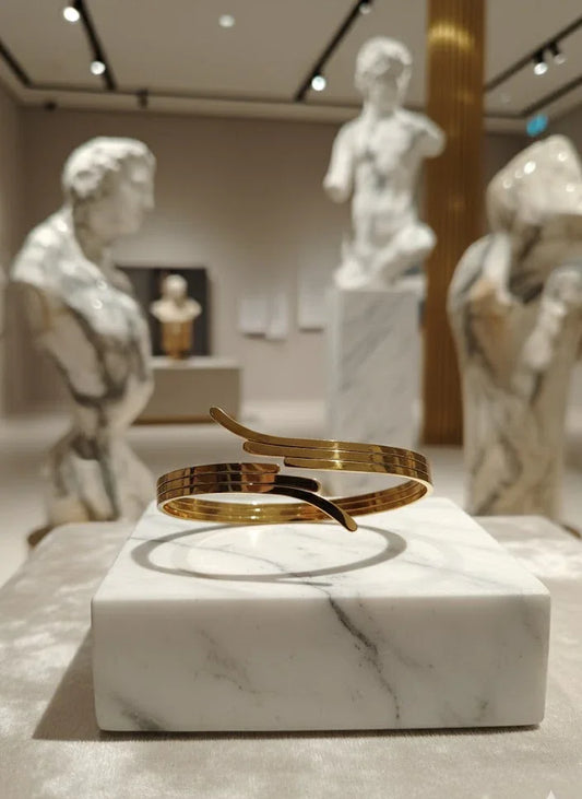 Gold bracelet on a marble pedestal with classical statues in the background
